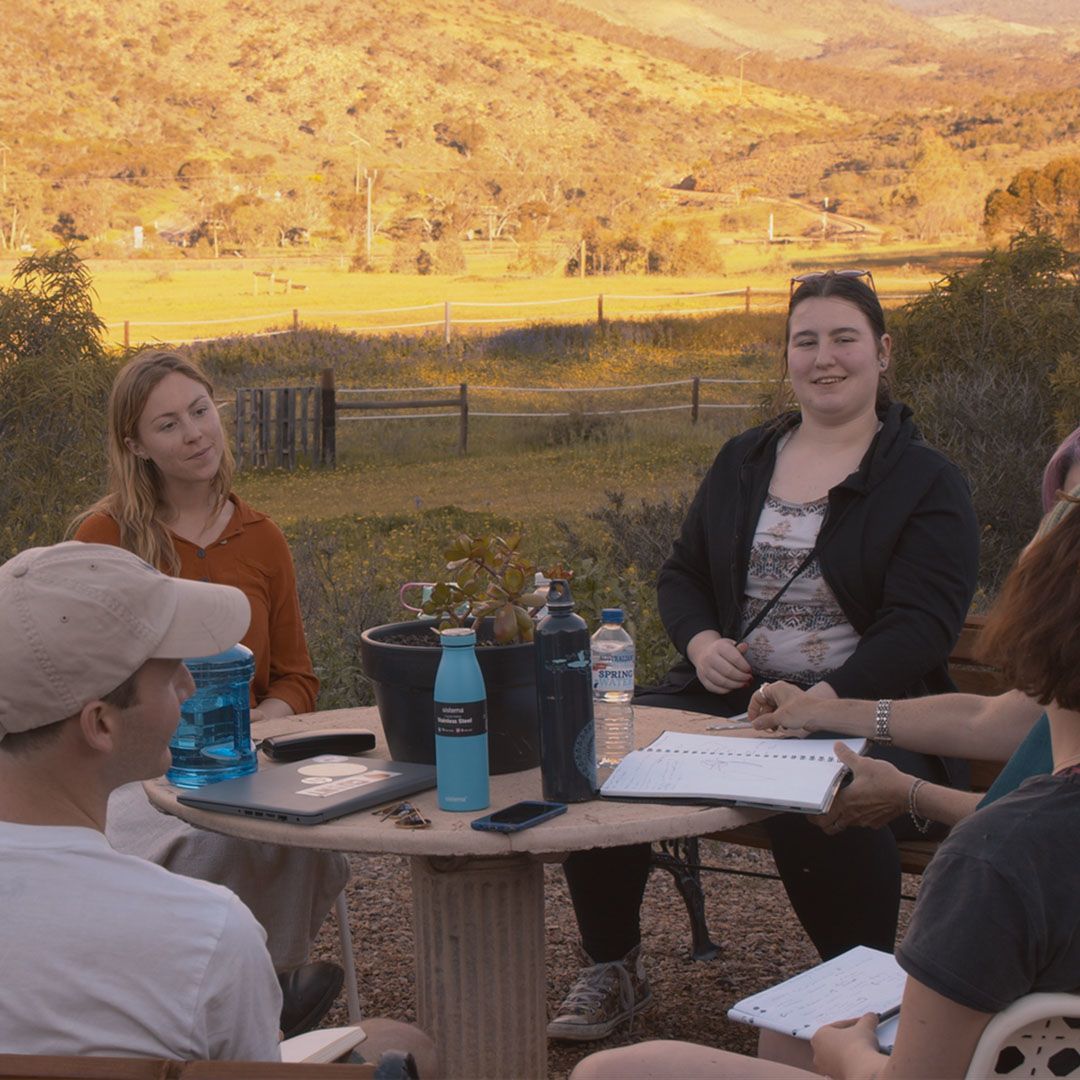 A group of young writers gathered around a table, conversing
